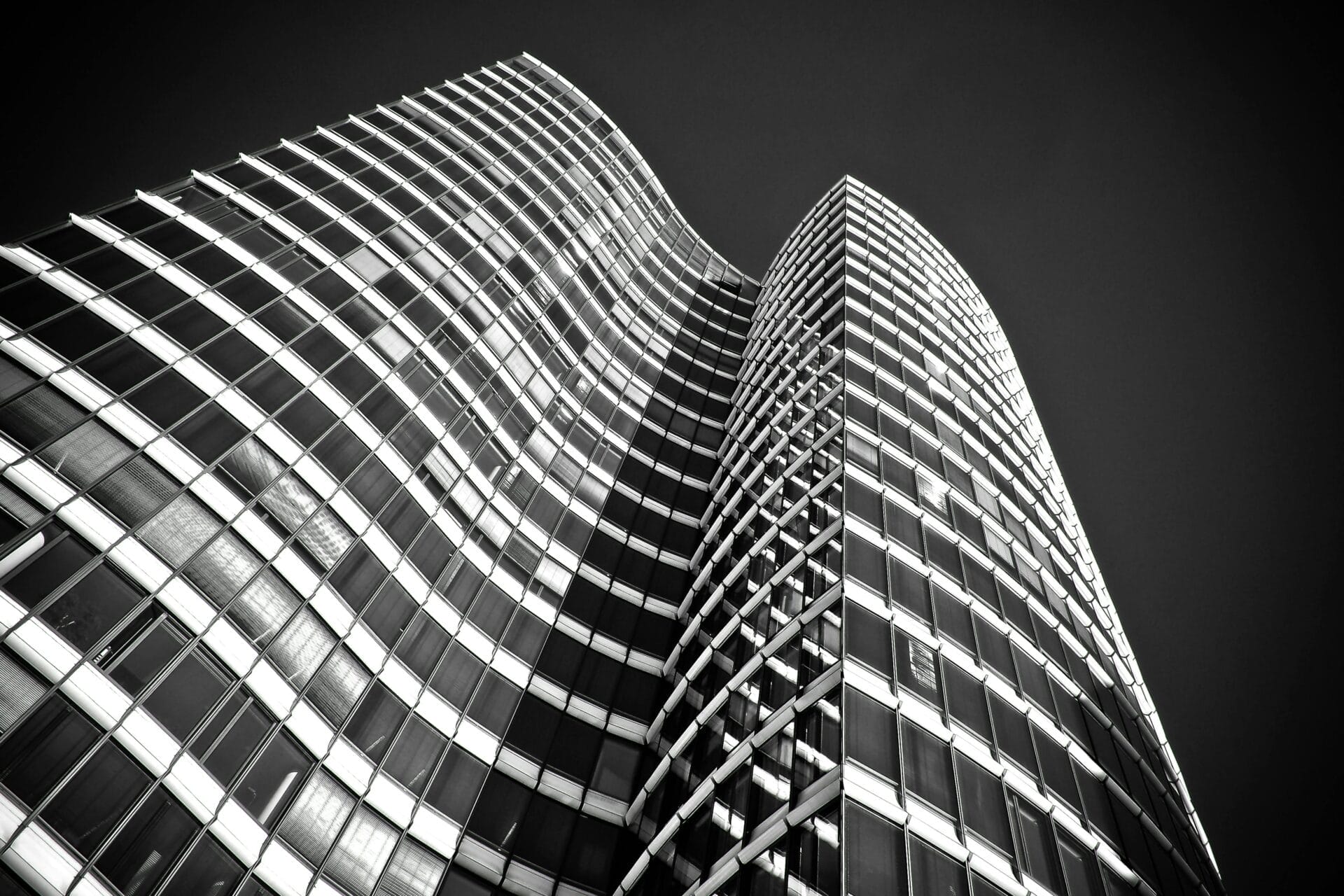 Black and white view of a modern skyscraper with a curved facade and grid-like window patterns.